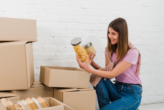 Free photo smiling young woman looking at snack bottles taken from the cardboard box