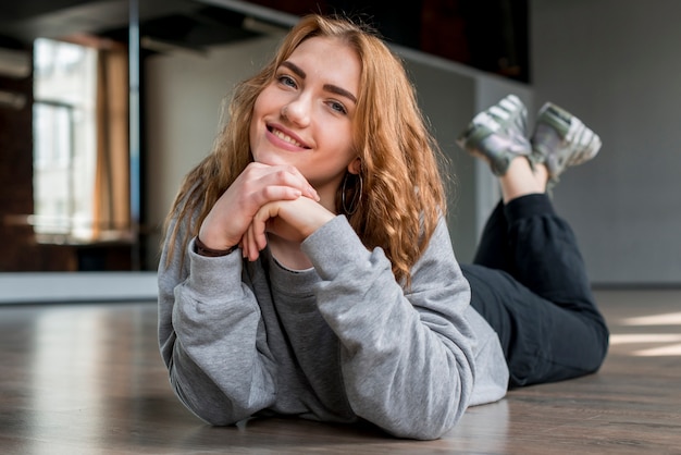 Free photo smiling young woman lying on floor looking at camera