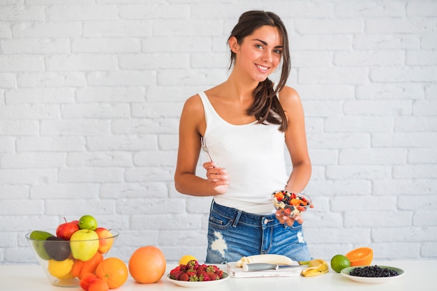 Giovane donna sorridente che produce macedonia di frutta fresca