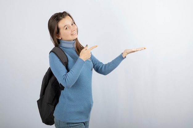 smiling young woman model with backpack pointing at a hand.