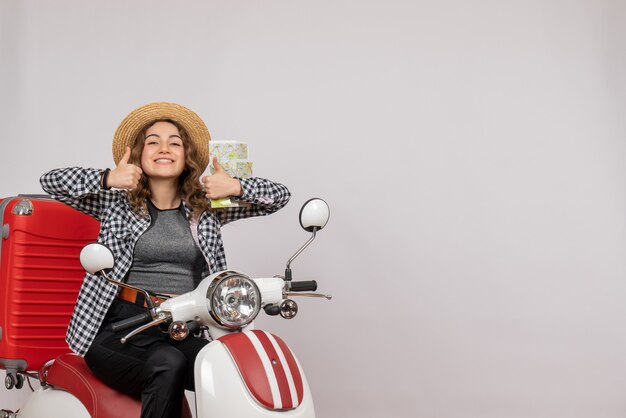 smiling young woman on moped holding card making thumbs up sign on grey