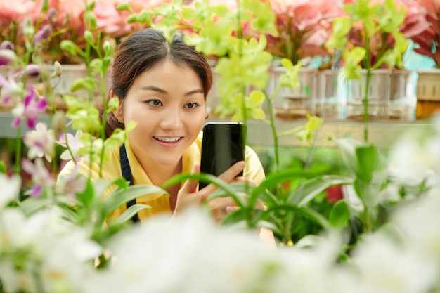 ソーシャルメディア​を​介して​販売する​ために​温室​で​花​を​撮影する​若い​女性​の​笑顔