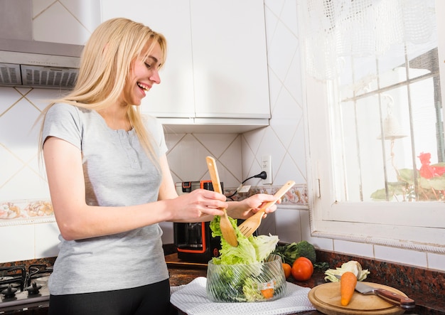 Smiling young woman picking up the lettuce leaf with wooden spatula