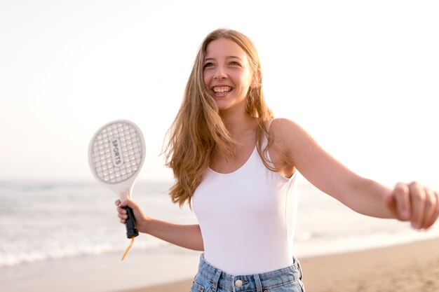 Улыбаясь молодая женщина, играя с ракеткой на пляже