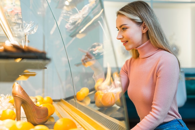 Smiling young woman pointing on a cake in a showcase