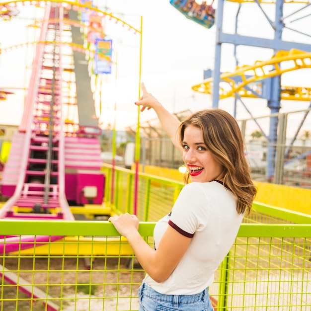 Smiling young woman pointing finger at roller coaster ride