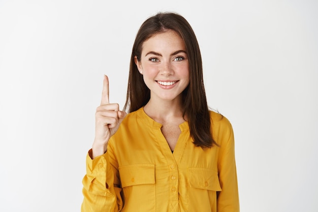 흰색 배경 위에 서 있는 이미지 위에 광고를 표시하는 손가락을 가리키는 웃는 젊은 여성