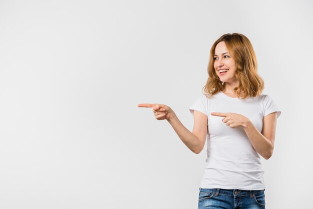 白い背景に対して指を指している若い女性の笑みを浮かべてください。