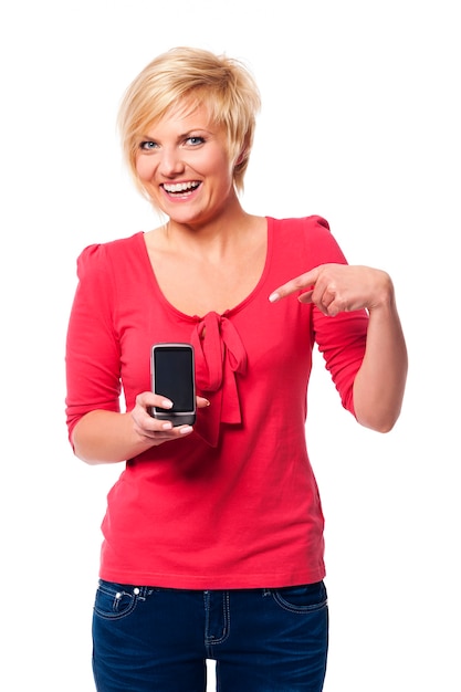 Foto gratuita giovane donna sorridente che indica allo schermo del telefono cellulare