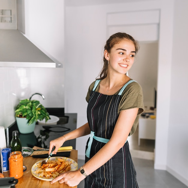 Улыбается молодая женщина готовит макароны на кухне