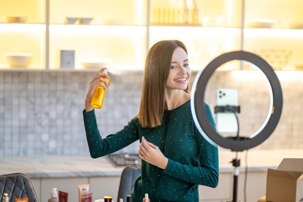 オンライン美容チュートリアル中にヘアスプレーを提示する笑顔の若い女性