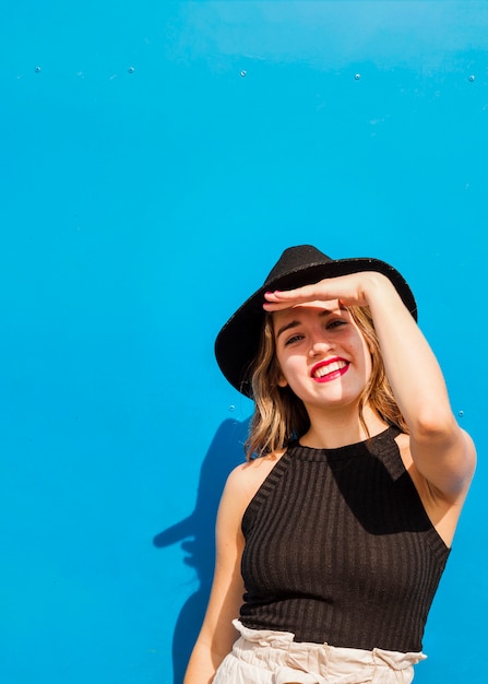 Smiling young woman put her hand on forehead to shield eyes from the sun