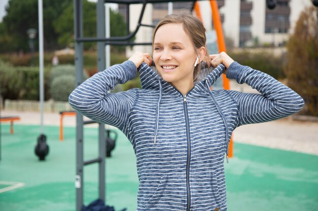 スポーツ地面にパーカーフードを入れて笑顔の若い女性