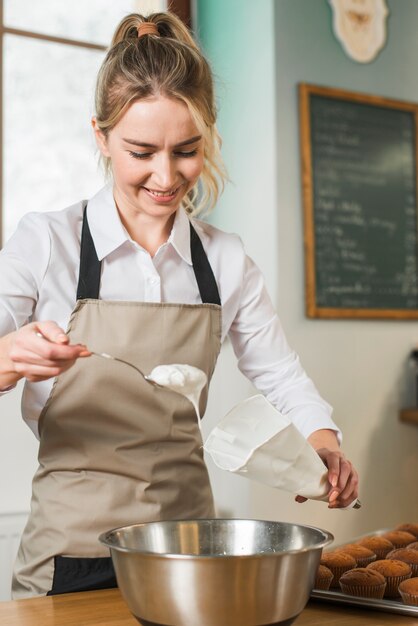 Smiling young woman putting white cream in the white icing bag