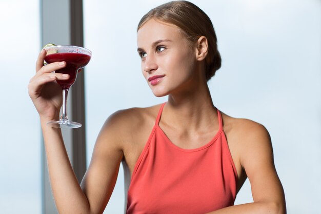 Улыбаясь молодая женщина, повышение стакан с коктейлем