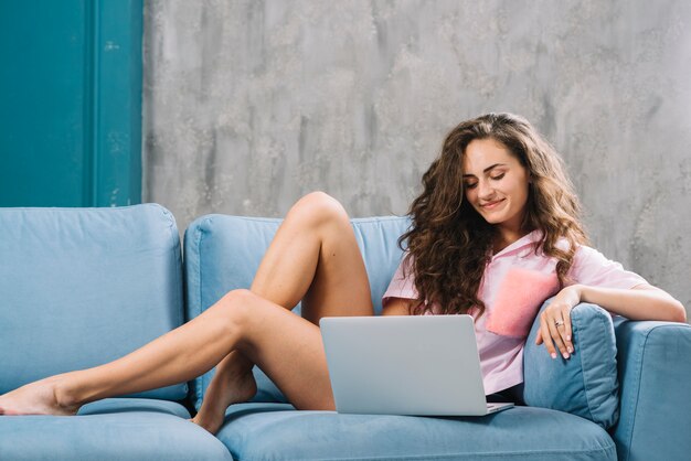 Smiling young woman relaxing on sofa using laptop