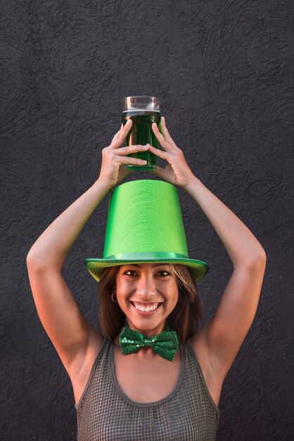 Smiling young woman in Saint Patricks hat holding glass of drink