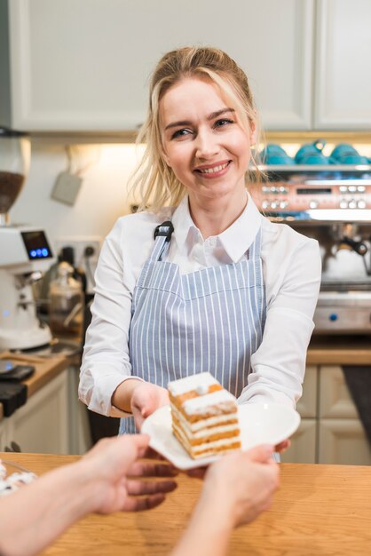 コーヒーショップで女性客にペストリーケーキを提供する若い女性の笑みを浮かべてください。