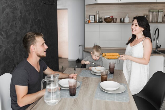 Smiling young woman serving steamed corn to her family at breakfast