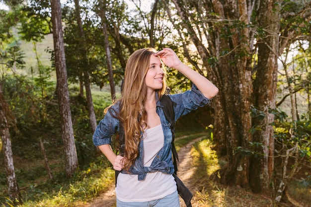 Free photo smiling young woman shielding her eyes in forest