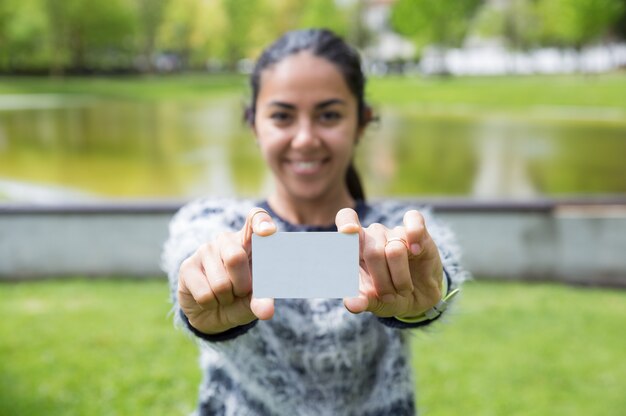 Smiling young woman showing blank plastic card in city park