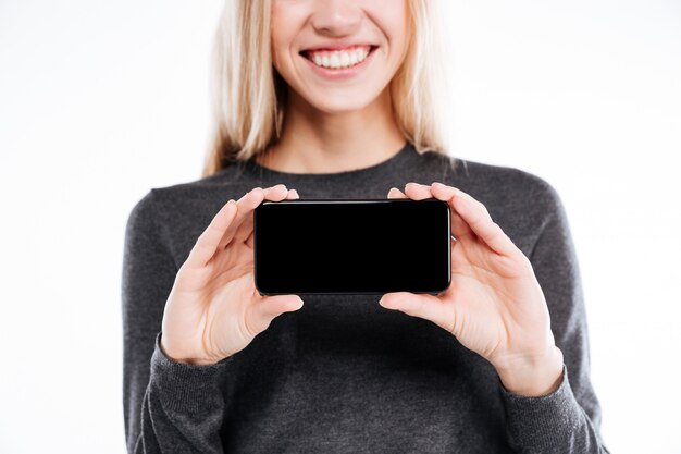 Ся молодая женщина показывая пустой экран мобильного телефона к камере