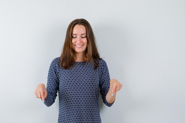 Smiling young woman showing down with his fingers on white background