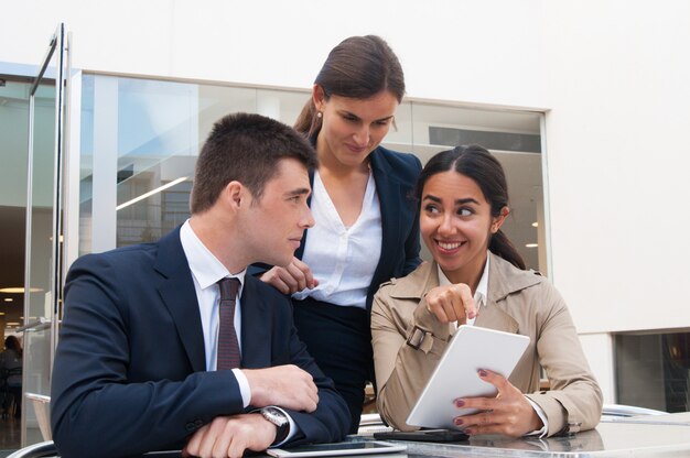 Smiling young woman showing tablet screen to business people