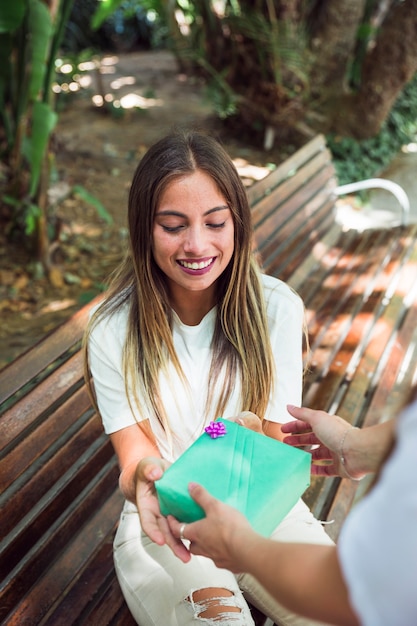 Free photo smiling young woman sitting on bench receiving gift from her friend