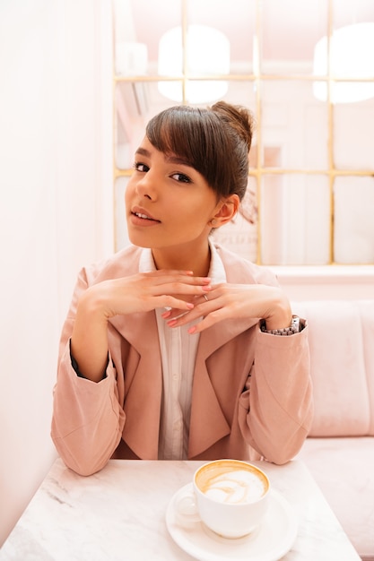 Smiling young woman sitting at cafe with cup of coffee