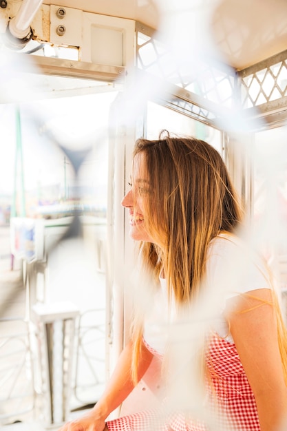 Free photo smiling young woman sitting in the ferris wheel cabin