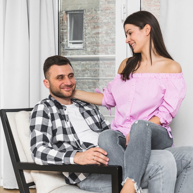 Smiling young woman sitting on her boyfriend's lap sitting on chair