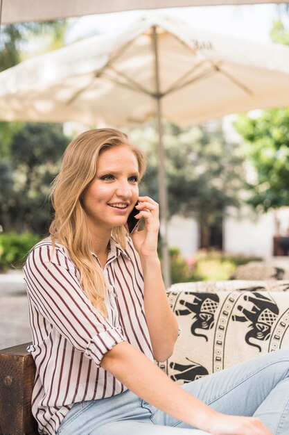 携帯電話で話している屋外に座っている笑顔の若い女性