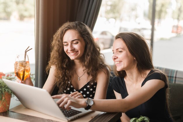 Smiling young woman sitting in restaurant looking at laptop