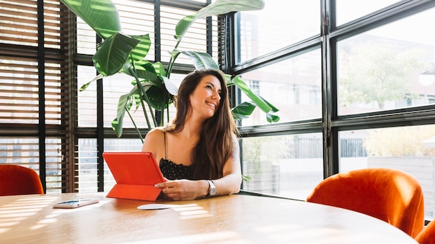 Foto gratuita giovane donna sorridente che si siede nel ristorante con la compressa digitale