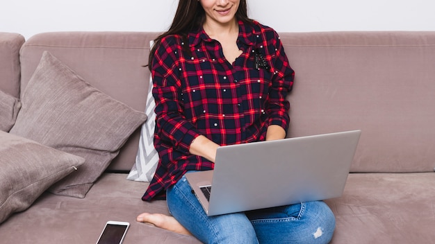 Free photo smiling young woman sitting on sofa using laptop