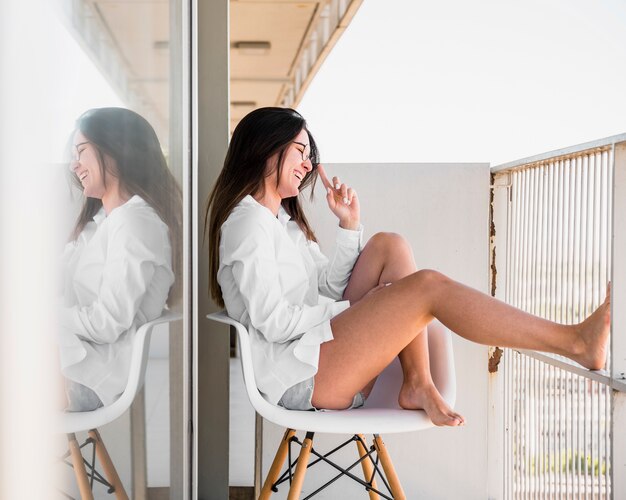 Smiling young woman sitting on white chair in the balcony