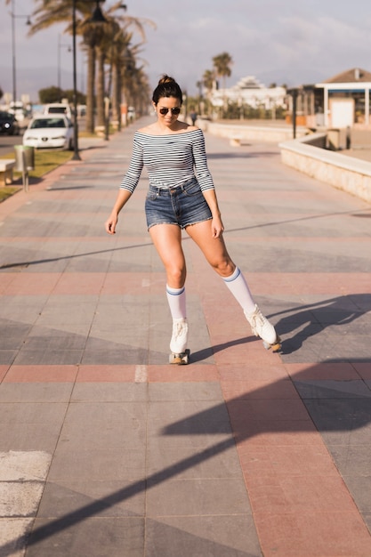 Улыбается молодая женщина, кататься на коньках на тротуаре в городе