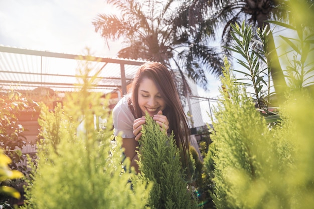 Smiling young woman smelling plant in greenhouse