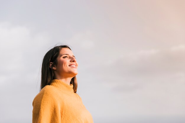 Smiling young woman standing against sky looking away