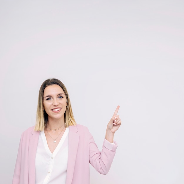 Smiling young woman standing against white background pointing upward