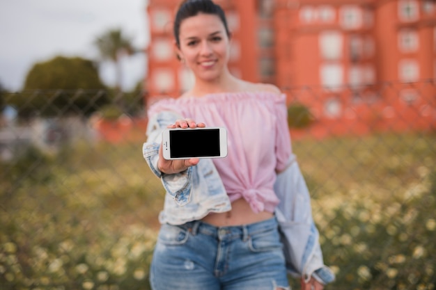 Smiling young woman standing in field showing her mobile phone