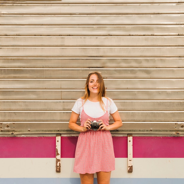 Foto gratuita giovane donna sorridente che sta davanti alla macchina fotografica della tenuta del ferro ondulato a disposizione