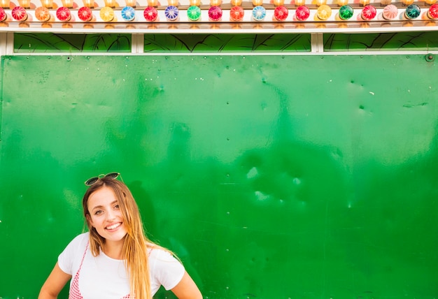 Smiling young woman standing in front of green wall decorated with colorful light bulb