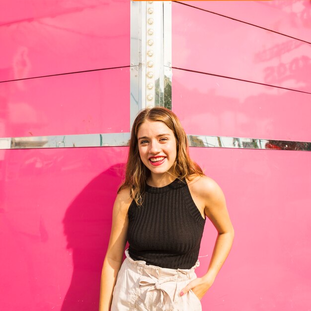 Smiling young woman standing in front of pink wall