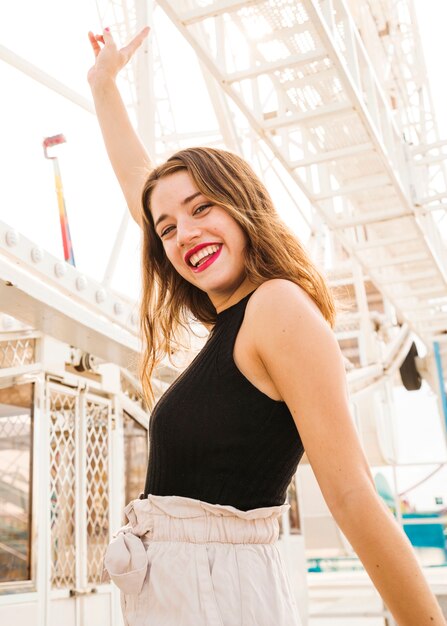 Smiling young woman standing in front of white ferris wheel gesturing