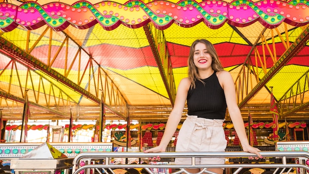 Foto gratuita giovane donna sorridente che sta dietro l'inferriata al parco di divertimenti