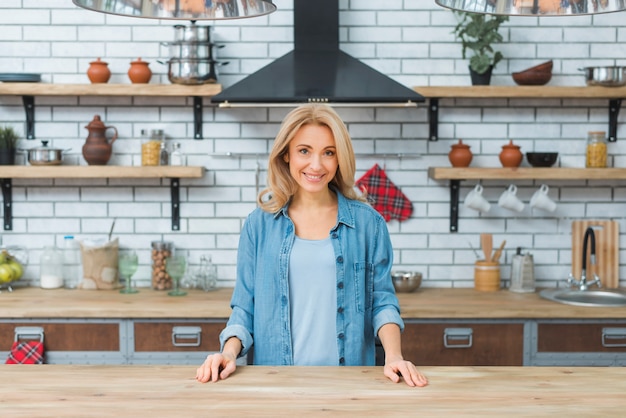 台所の木製のテーブルの後ろに立っている笑顔の若い女性