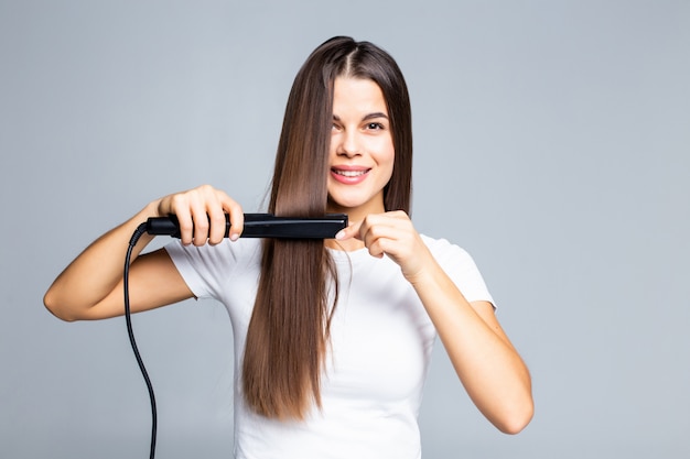 Smiling young woman straightening her hair with white