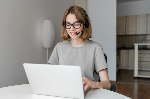 인터넷에서 온라인 교육 과정을 학습하기 위해 노트북을 사용하는 젊은 여자 학생 착용 무선 헤드셋 미소